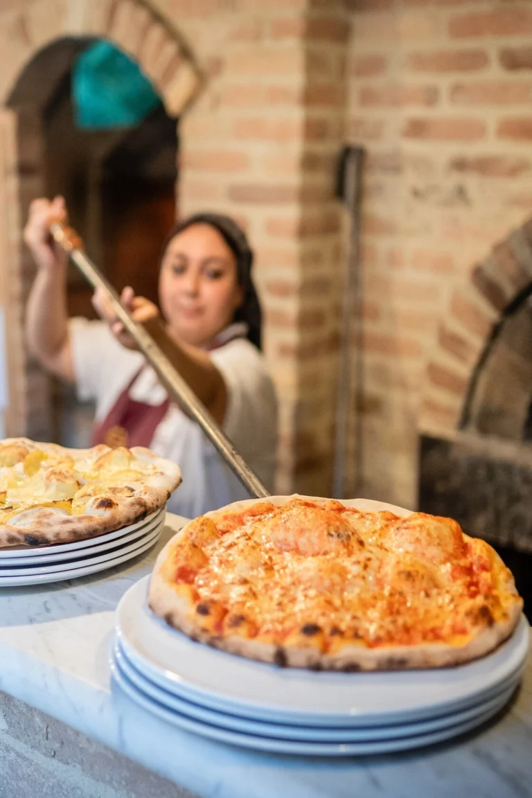 pizzaiola sforna pizze appena tolte dal forno a legna del ristorante pizzeria del castello di baccaresca
