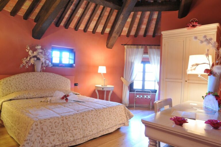 Camera Junior suite del castello con molta luce e travi a vista con muri di colore arancione e mobili chiari