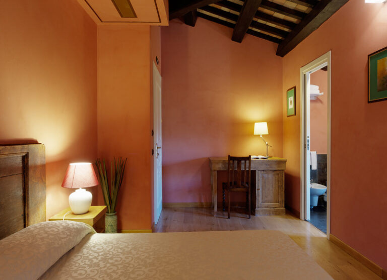 Camera deluxe del castello di baccaresca Umbria con scrivania illuminata letto in primo piano con luci accese e scorcio del bagno a destra