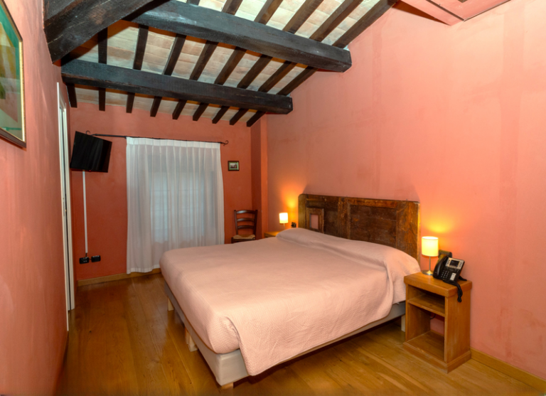 Camera deluxe del castello di baccaresca gubbio con travi di legno a vista nel soffitto televisione a muro letto matrimoniale e finestra a lato