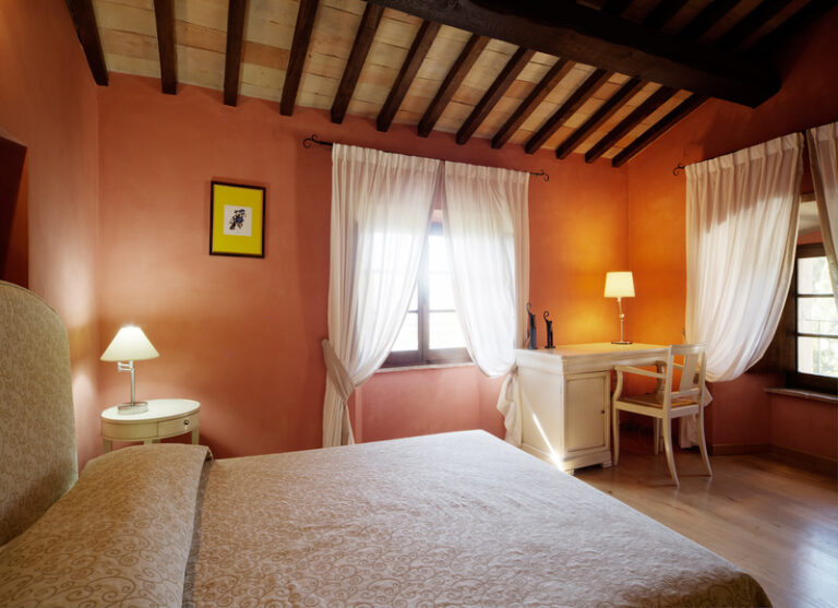 Deluxe room del castello di baccaresca con quadro giallo nella parete frontale letto in primo piano e due finestre nello sfondo travi a vista nel soffitto