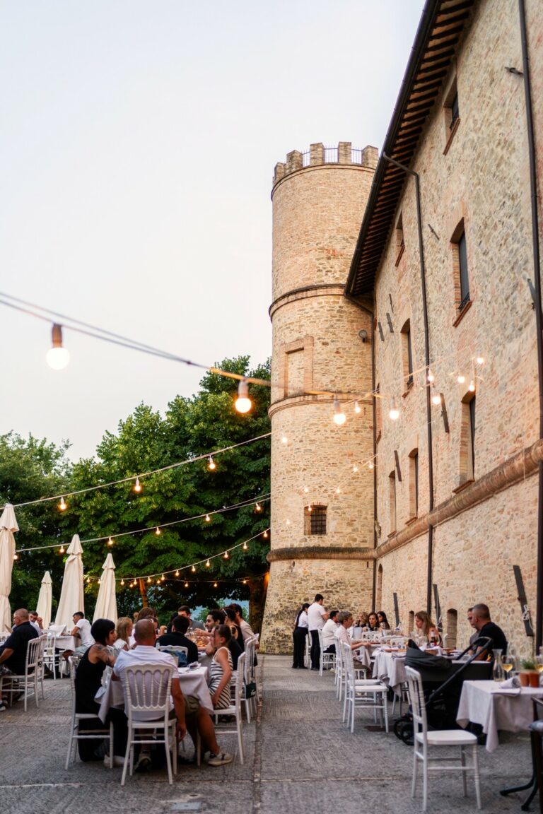 ristorante pizzeria del castello di baccaresca con tavoli all'aperto ai piedi del castello medievale e luci accese per serate e cene