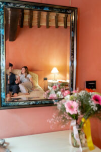 Coppia che sorseggia dei calici nel letto di una junior suite del castello di baccaresca con specchio e vaso di fiori in primo piano