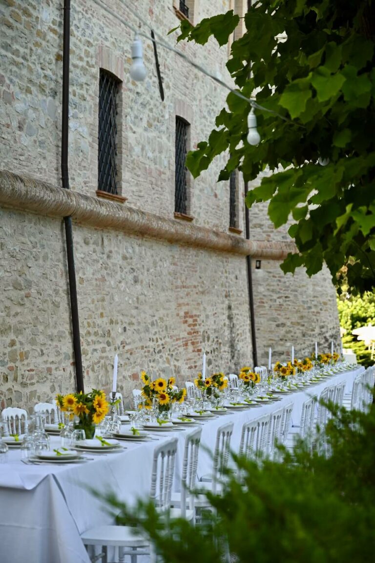 evento privato con tavolata lunga a ridosso delle mura del castello di baccaresca con girasoli e candele che decorano l'evento