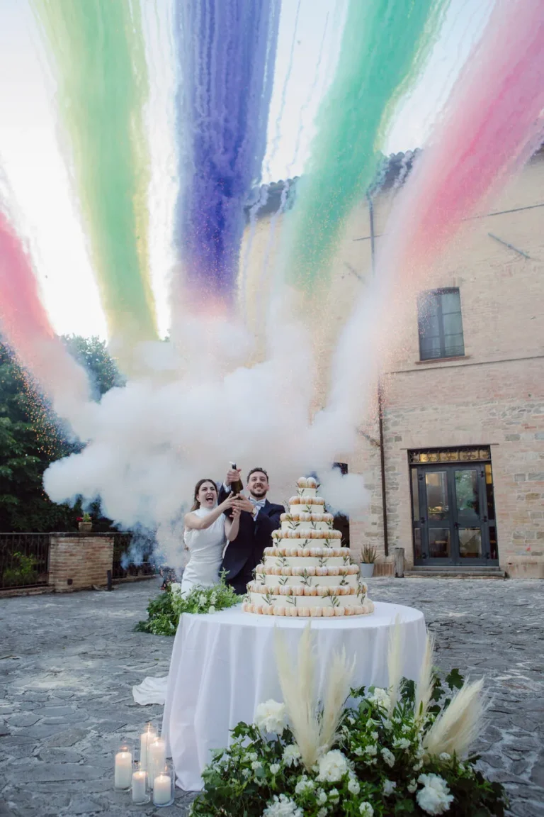Taglio della torta nuziale al Castello di Baccaresca a Gubbio con fumogeni colorati arcobaleno durante un destination wedding in Umbria.