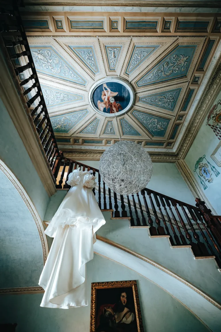 Abito da sposa appeso allo scalone storico con soffitto affrescato all'interno del Castello di Baccaresca, esclusiva wedding venue in Umbria.
