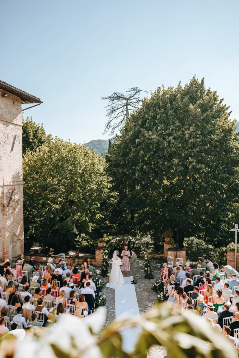 Cerimonia simbolica di matrimonio all'aperto nella corte del Castello di Baccaresca a Gubbio con invitati e arco floreale