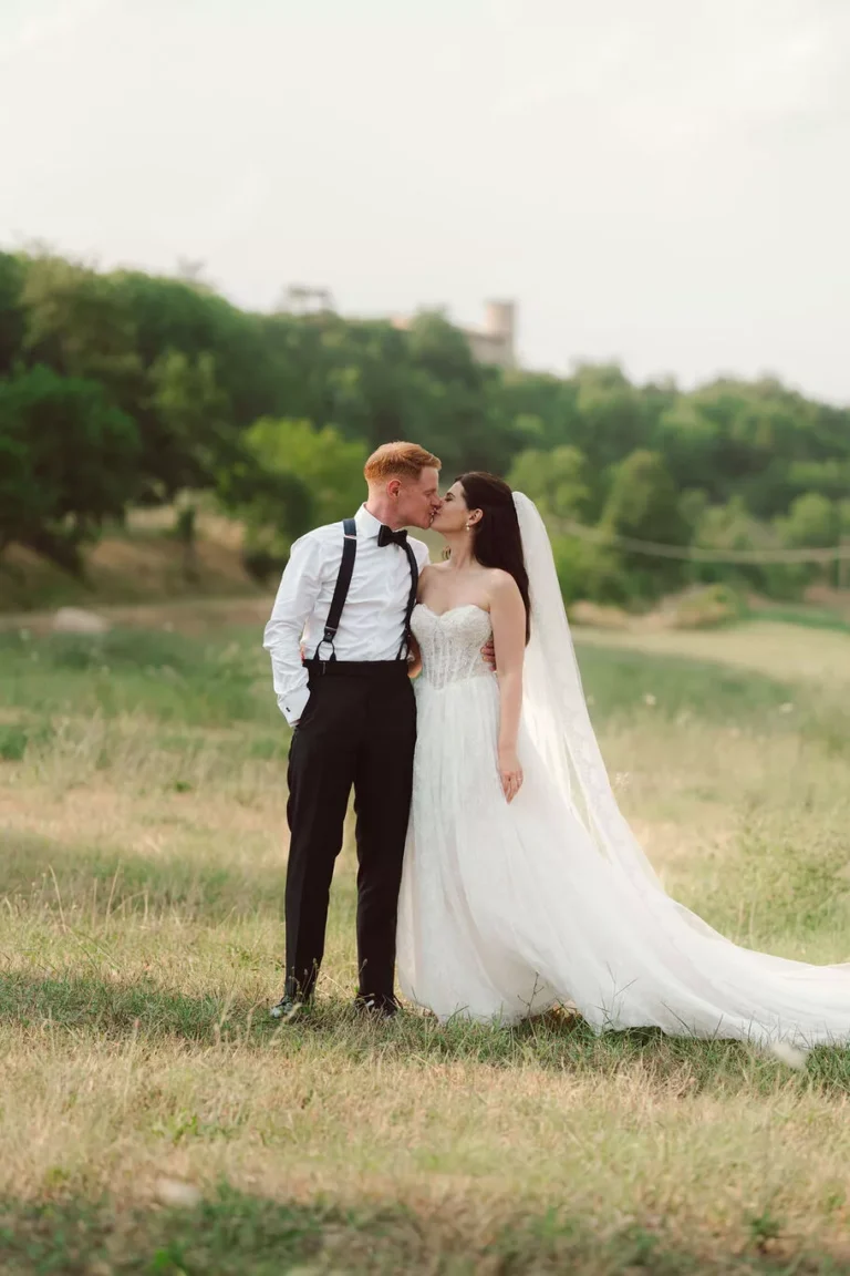 Sposi si baciano in un prato verde nelle campagne di Gubbio con il Castello di Baccaresca sullo sfondo durante un matrimonio in Umbria